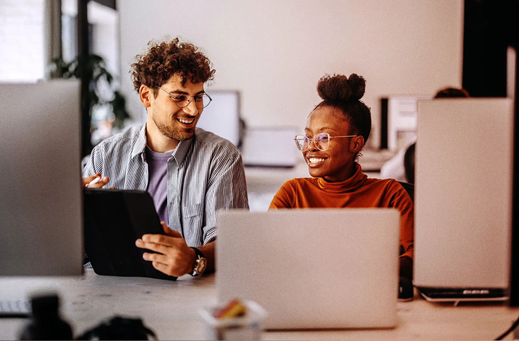 Two colleagues happily chatting at their desks  