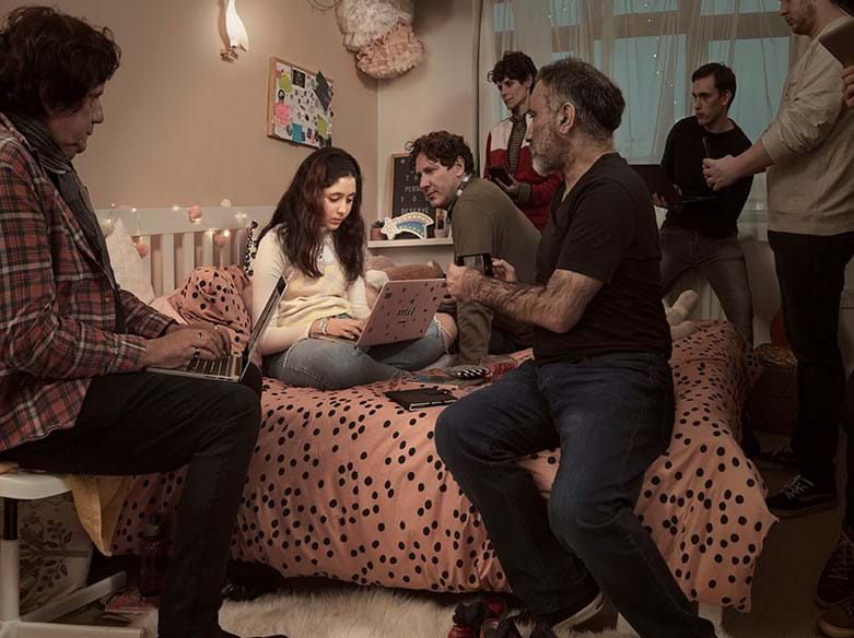 Child with laptop and several adults with phones in a bedroom