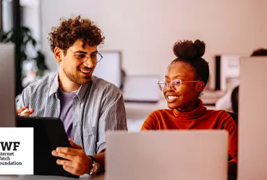 Two colleagues on computers laughing together in an office