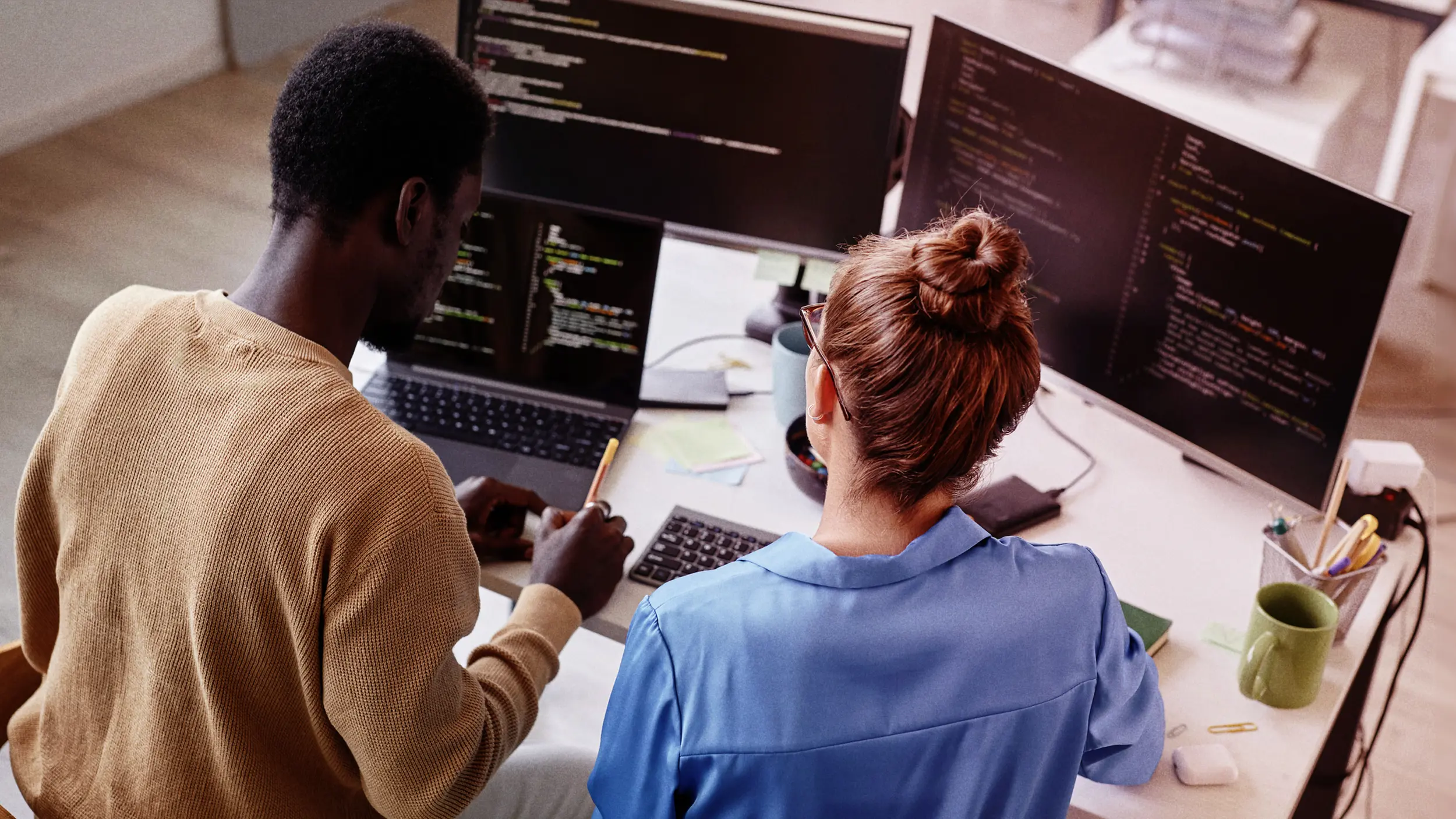 Two people sitting at a desk looking at code on a computer screen