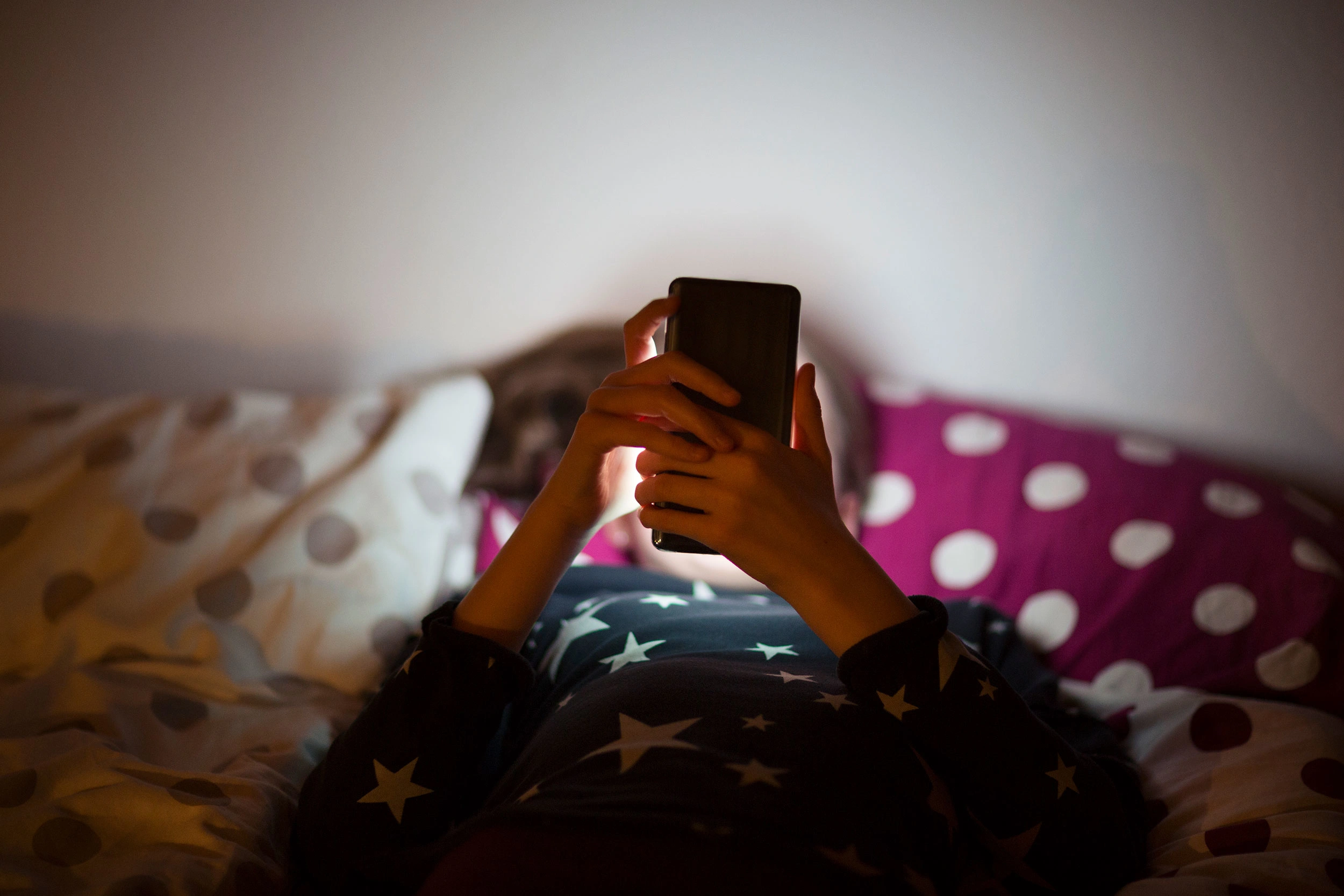 Child looking at phone on bed