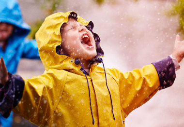 Happy child in the rain with yellow rain coat